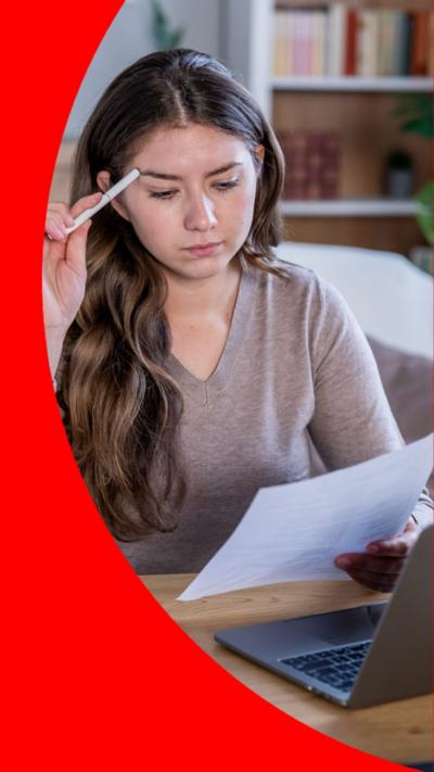 A woman looks down at a piece of paper she is holding. She holds a white pencil to her forehead.