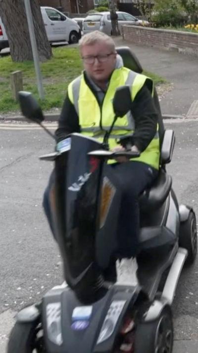 Josh Howell crossing the road on a mobility scooter while wearing a high-vis jacket.