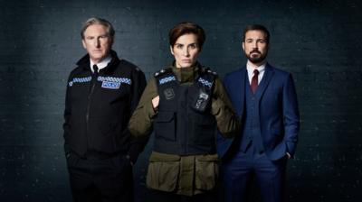 Line of Duty characters Ted, Kate and Steve pose together. Ted and Kate wear police uniforms, while Steve wears a blue suit