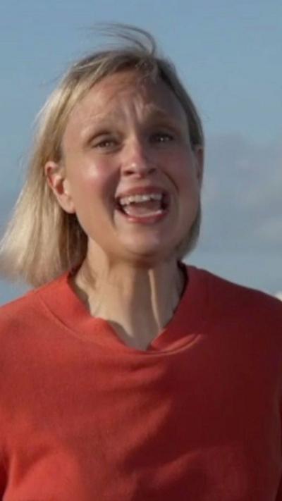 A woman wearing a red top reacts towards the camera.