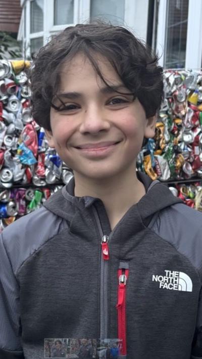 A young boy with black hair and a grey jacket stood in front of crushed cans