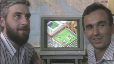 Creators Peter Molyneux and Les Edgar being interviewed either side of a screen showing the video game.