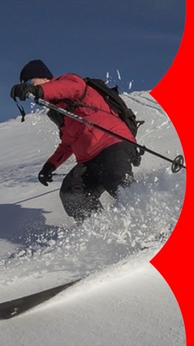 A man dressed in a red jacket and black trousers skis down a snow covered hill