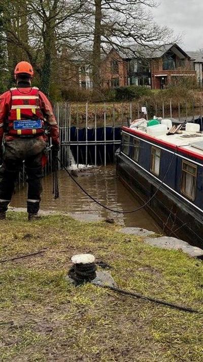 A narrowboat is refloated on a canal. An engineer in waterproof safety clothing is standing by