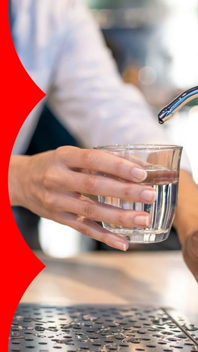 A waiter fills a glass with water from a tap