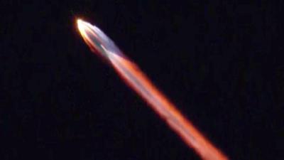 A multicoloured stream of light emanates from a rocket in the night sky.