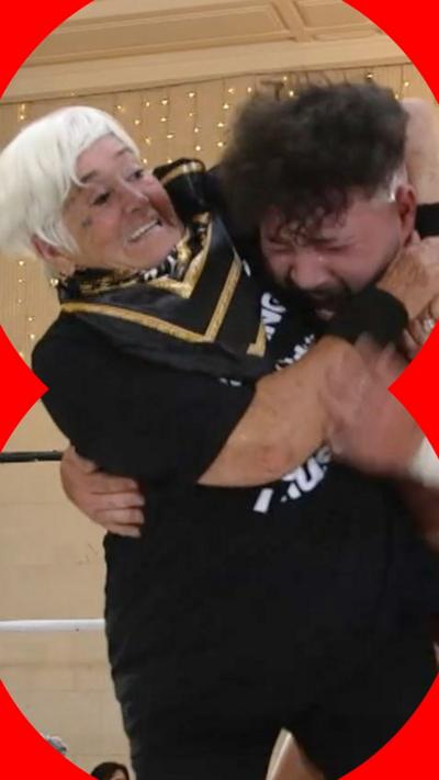 A woman with short, white hair has a man in a headlock