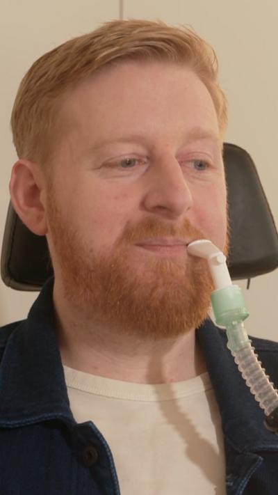 Michael has ginger hair and beard. He has a white breathing tube near his face.