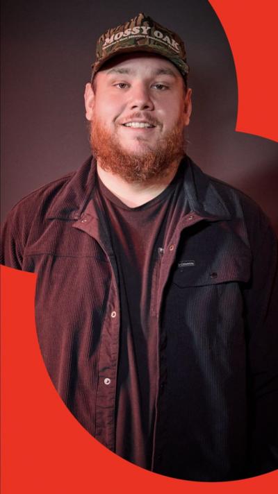 A man, Luke Combs, wearing a black shirt and baseball cap, smiling to camera. He has a beard.