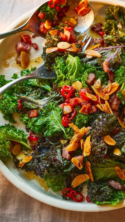 A light coloured plate with cooked kale, bacon, chilli and almonds.
