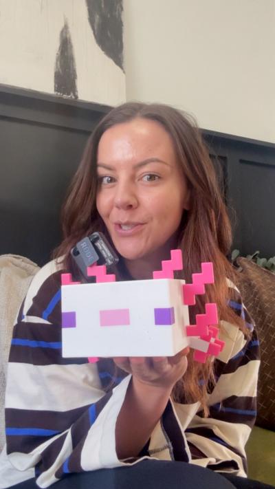 Tink Llewellyn who has long brown hair holding up a minecraft axolotl