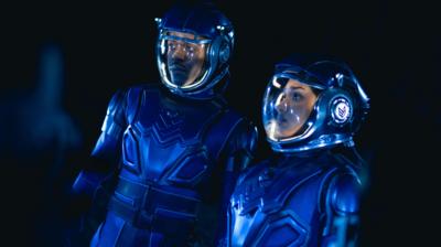 Two people wear blue helmets with a glass cover and blue armour suits
