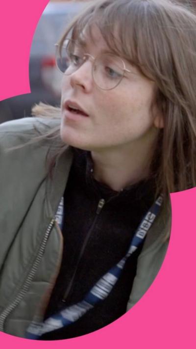 Lauren is wearing a green bomber jacket. She is standing outside a front door on a driveway.