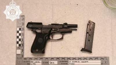 A gun is photographed next to a ruler with measurements. The photograph, taken by police, has the force logo on it.