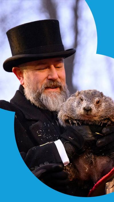 Groundhog handler AJ Dereume, wearing a black top hat and black coat, holds Punxsutawney Phil