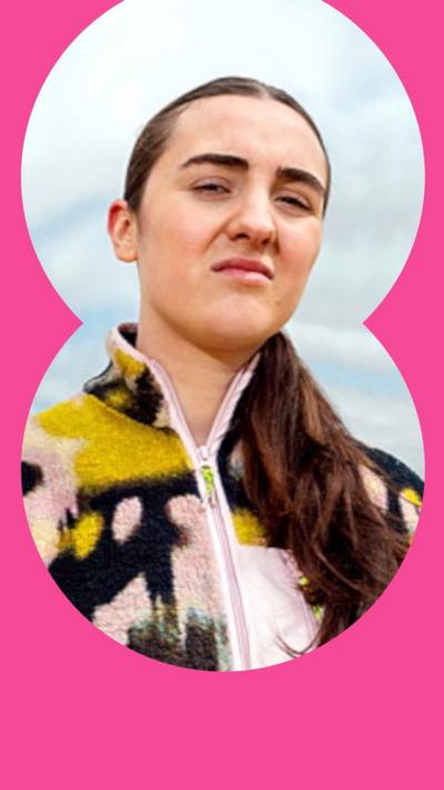 A woman with brown tied back hair and a scorn on her face looks down at the camera.