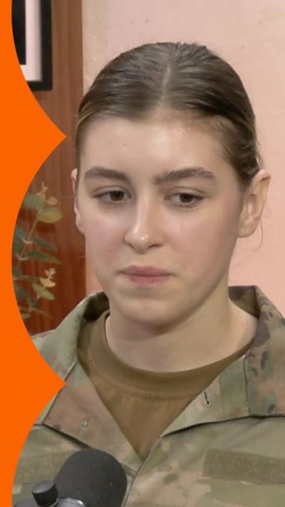 Sophia wears camouflage military uniform and sits in a podcast studio