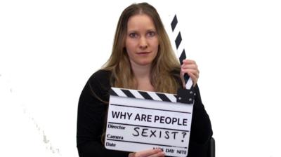 A woman holds a clapper-board saying "Why are people sexist?"