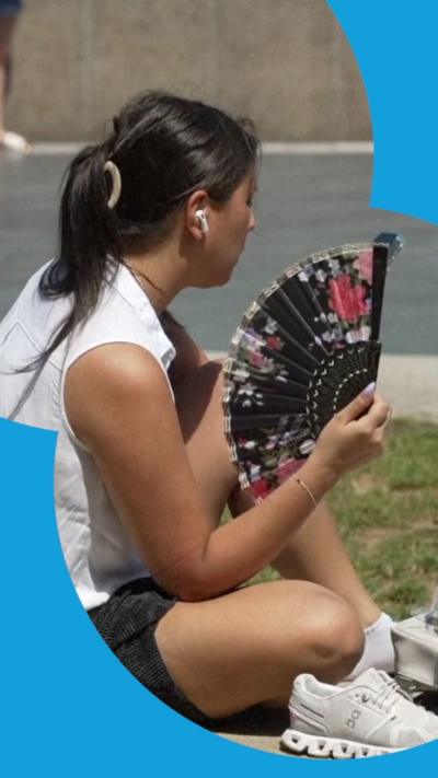 A woman fans herself while sitting in the heat.