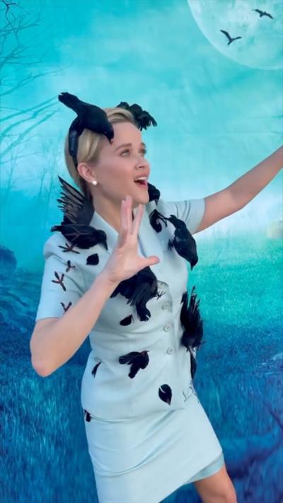 Reese Witherspoon dressed as the lead character from The Birds, wearing a pale blue suit covered with black birds.