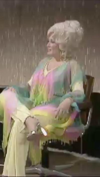 Dolly Parton sitting in chair in multi-colored shirt