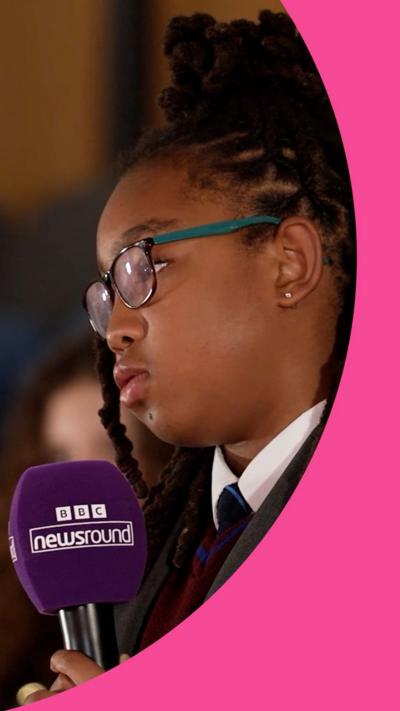 A girl with black braids and glasses holds a purple microphone