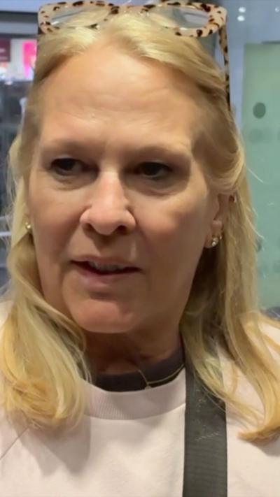 A woman speaks to the camera outside of airport arrivals