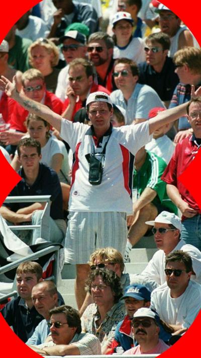 An England fan stands in a crowd with his arms outstretched in 1998