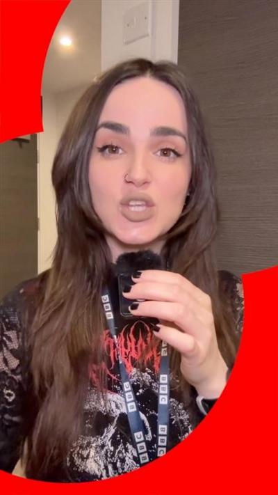 Woman with long dark brown hair holding a small microphone, looking straight at the camera