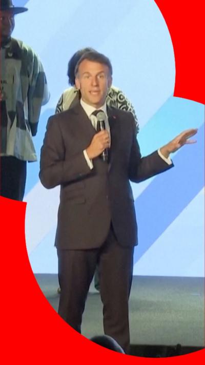 A man in a suit stands on a stage and speak to an audience