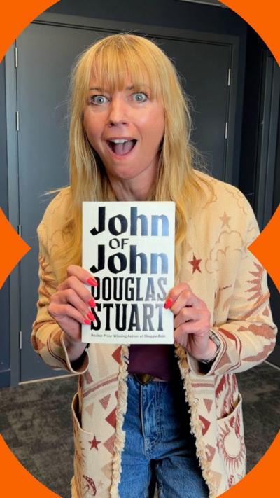 Sara Cox smiles at the camera while holding a book 