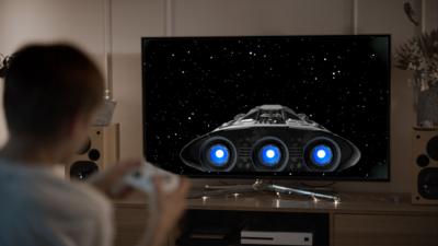 Boy playing video game with a spaceship on screen. 