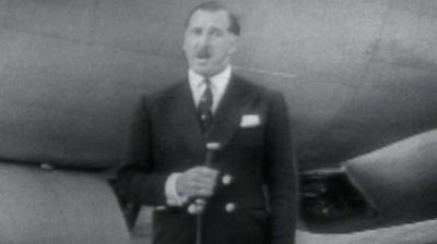 BBC presenter with a microphone stands in front of a plane