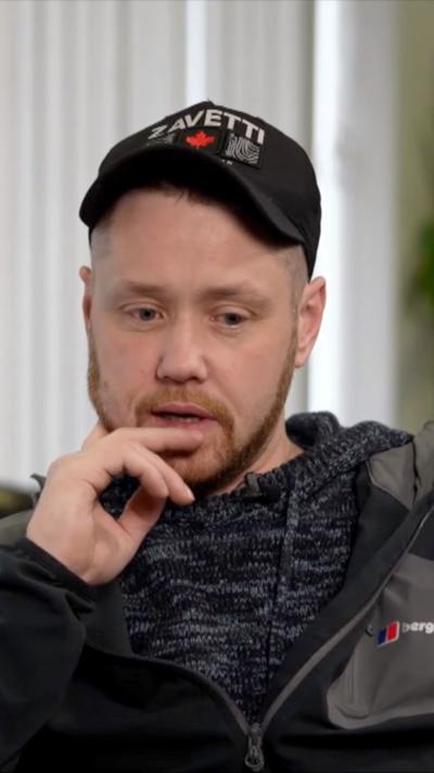 A man wearing a black baseball cap and black and grey tracksuit top.