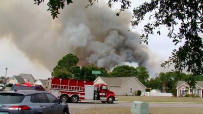 A fire truck is seen on a residential street as a plume of smoke is seen rising from behind homes