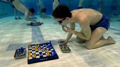 A man strokes his chin underwater while playing chess.