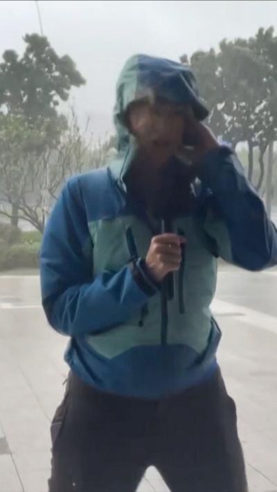 Laura Bicker, wearing a blue jacket, is blown by wind and rain.