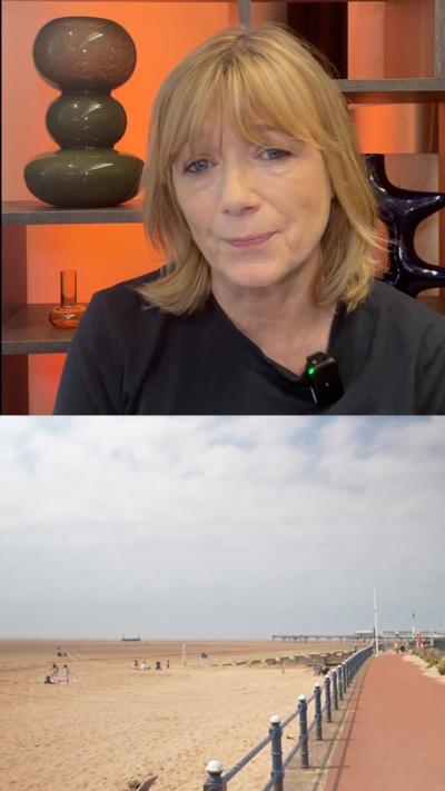 Woman with blonde hair and fringe wearing black t-shirt. Below a beach picture with blue skies.