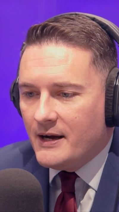 A man in a blue suit, light blue shirt and red tie wearing headphones talking into a microphone