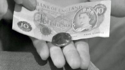 A black and white image of a hand holding a new 50p coin on top of an old ten-shilling note.