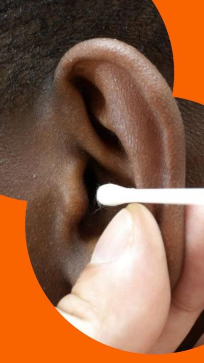 A boys ear is held by the finger of a doctor who is positioning a cotton bud near the ear canal.