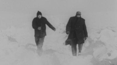 Two people walk through snow