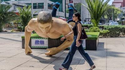 A woman walks in front of a toppled statue of a World Cup player.