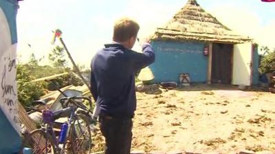 Christian Fraser pointing at thatched home