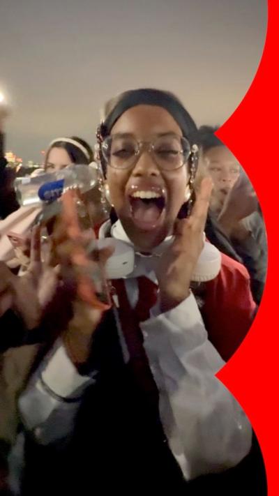 
A young woman mid scream, with both hand close to her face, in a crowd of people.