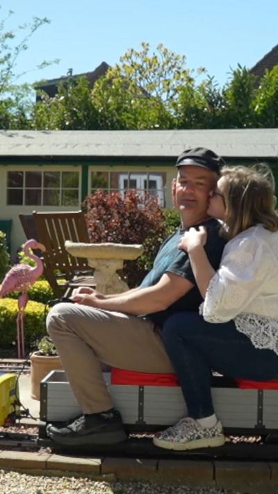 Man and woman sat on a little train in their garden. 
