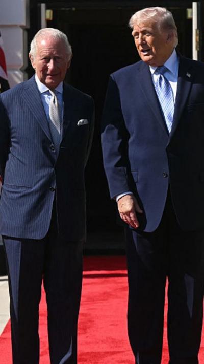 King Charles and President Donald Trump, both in blue suits, stand side-by-side outside the White House standing on a red carpet.