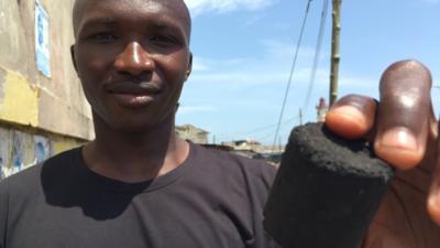 Slamson Ghana's Managing Director, Sampson Sayibu, holding a charcoal shape made from recycled human poo