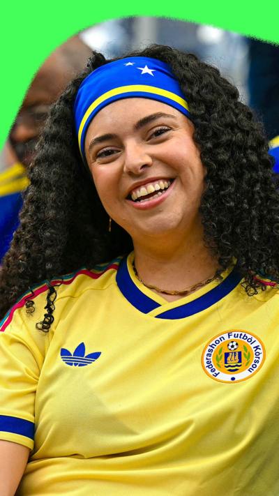 A Curacao fan smiles. She's wearing the team's yellow shirt.