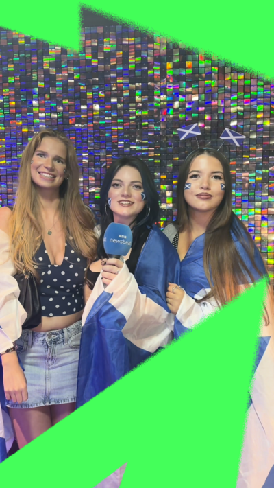 Three young women draped in Saltire flags in front of a mirrored backdrop